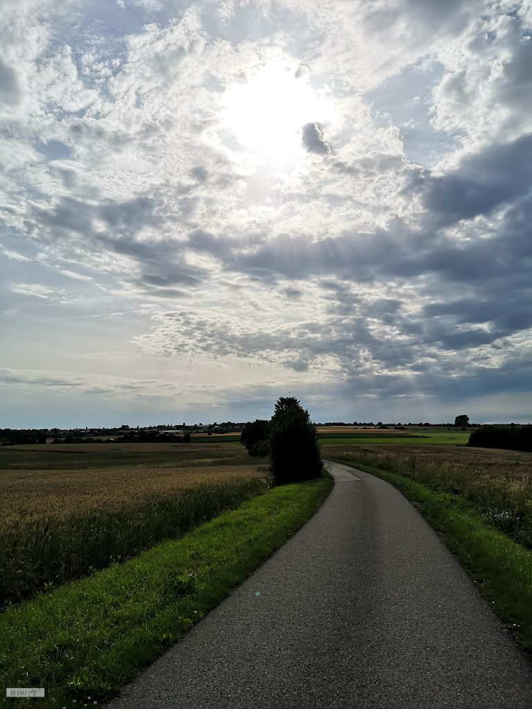 Straße und von der Sonne beschienener, wolkiger Hinmel